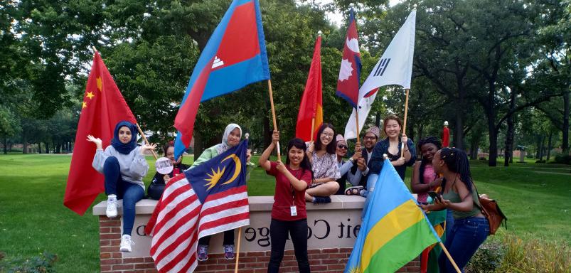 毕业典礼结束后，国际学生在十大菠菜台子的标志前挥舞着他们的旗帜...